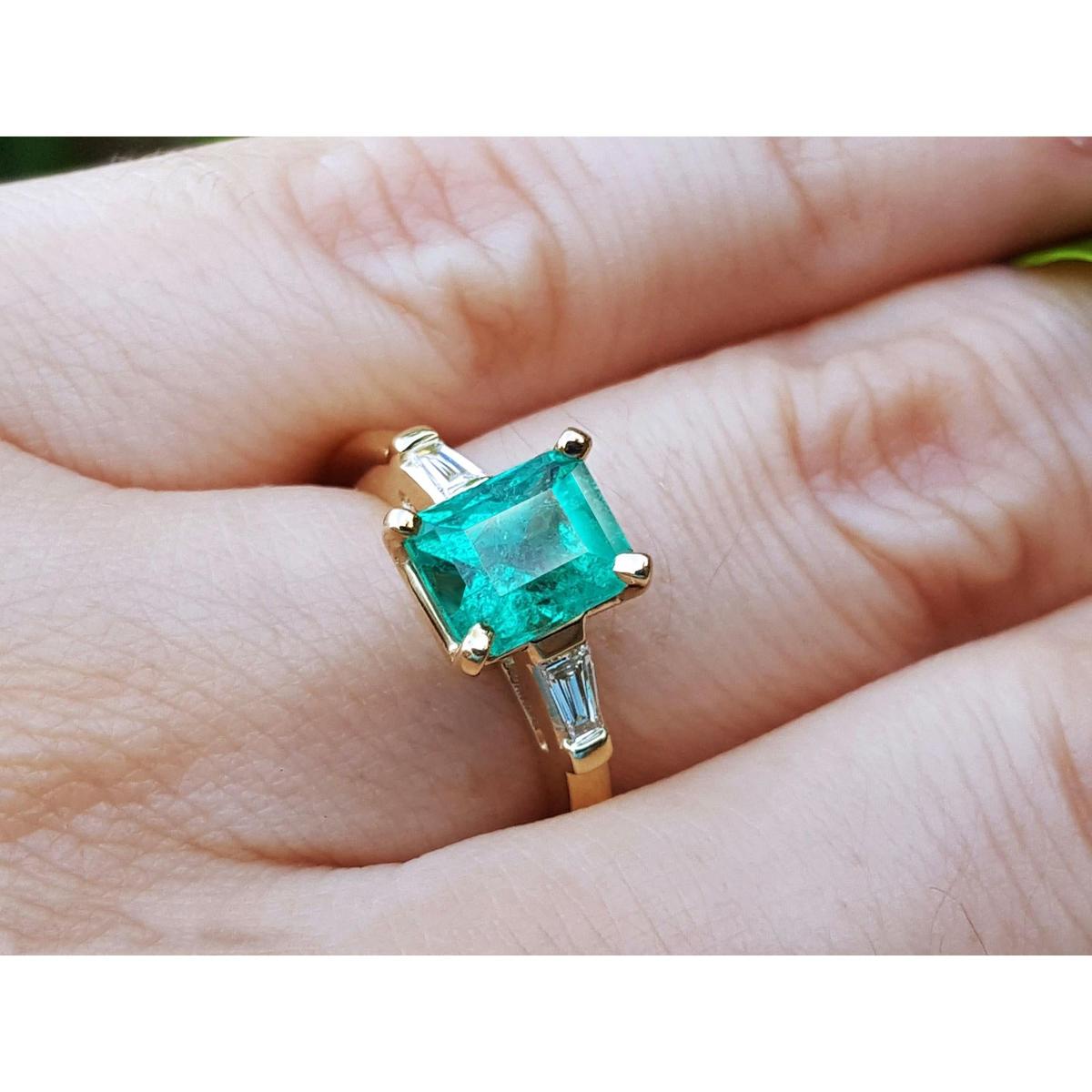 Gold ring with a natural Colombian emerald and side diamonds on a hand.