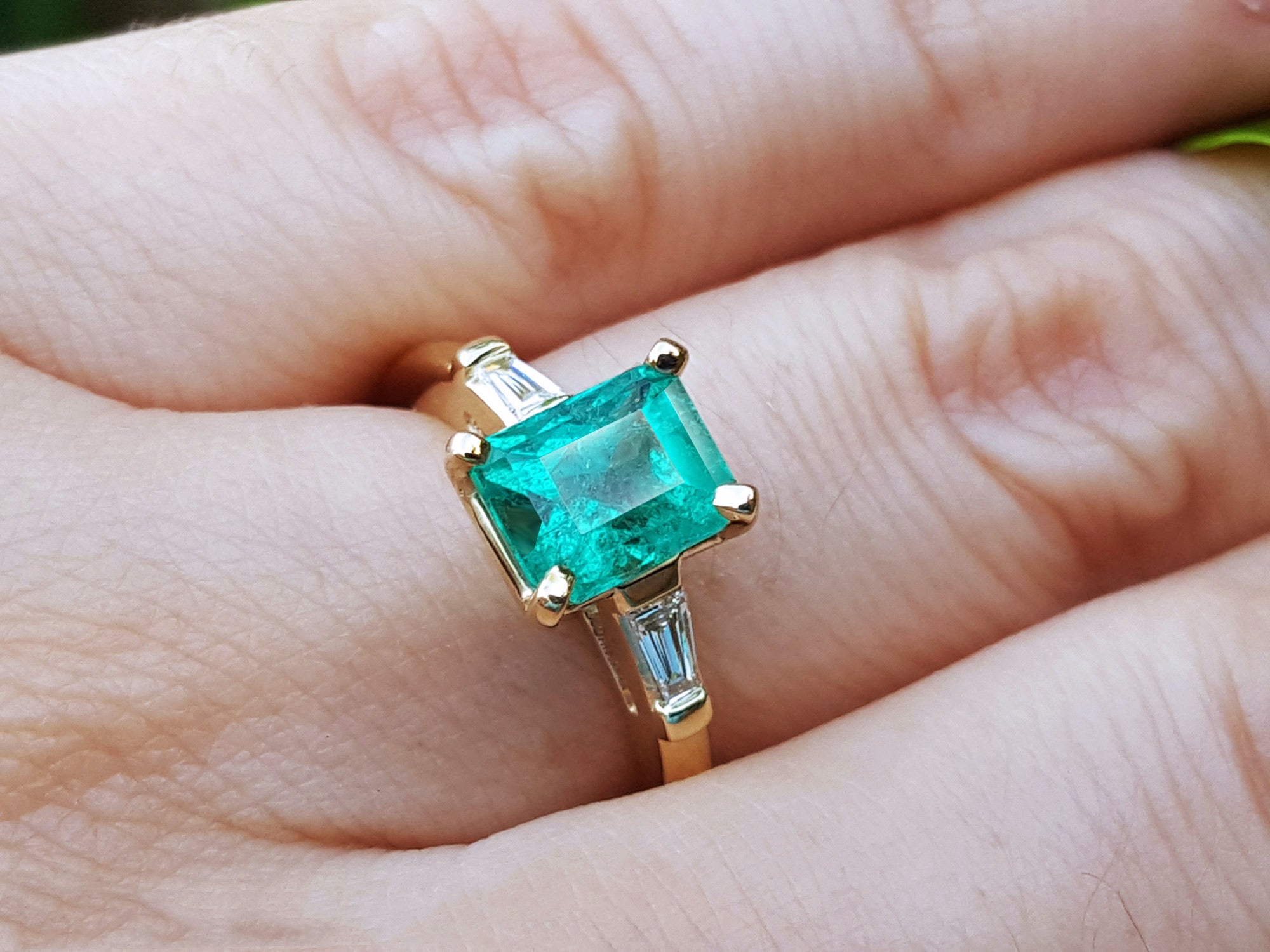Gold ring with a natural Colombian emerald and side diamonds on a hand.