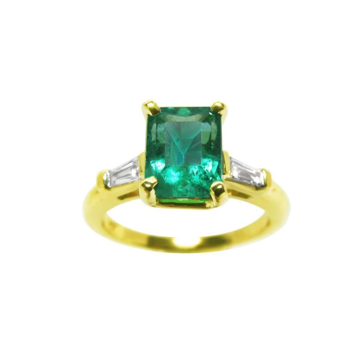 A front top view of an emerald gold ring with tapered baguettes side diamonds on a white background.