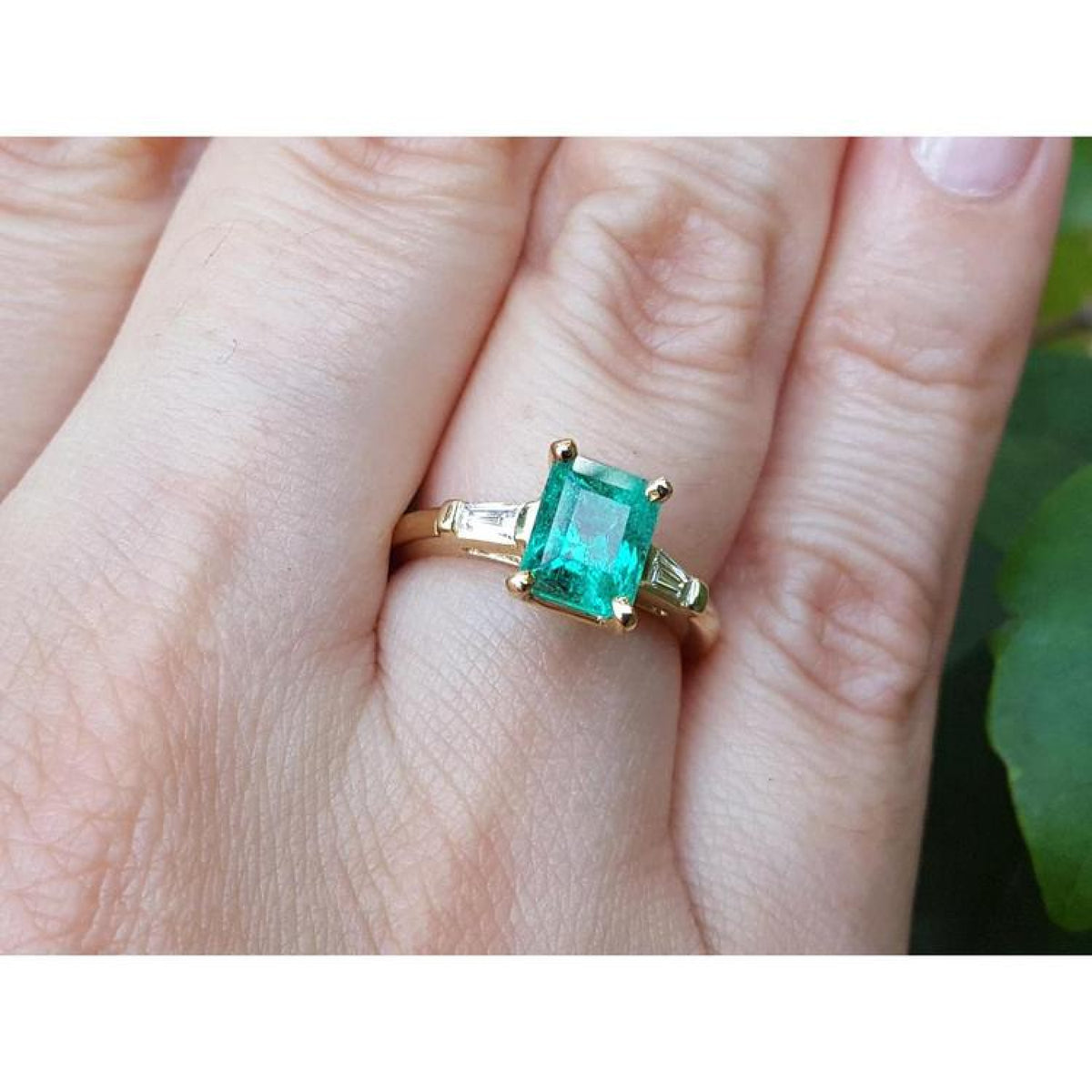 14K gold ring with a rectangular emerald-cut emerald and tapered baguette side diamonds on a hand.