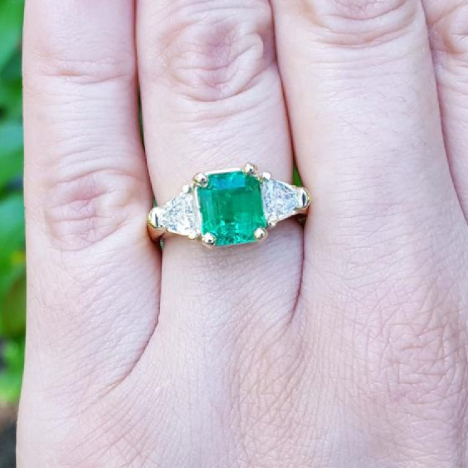 18K yellow gold ring with a GIA certified emerald and side trillion diamonds on a hand.