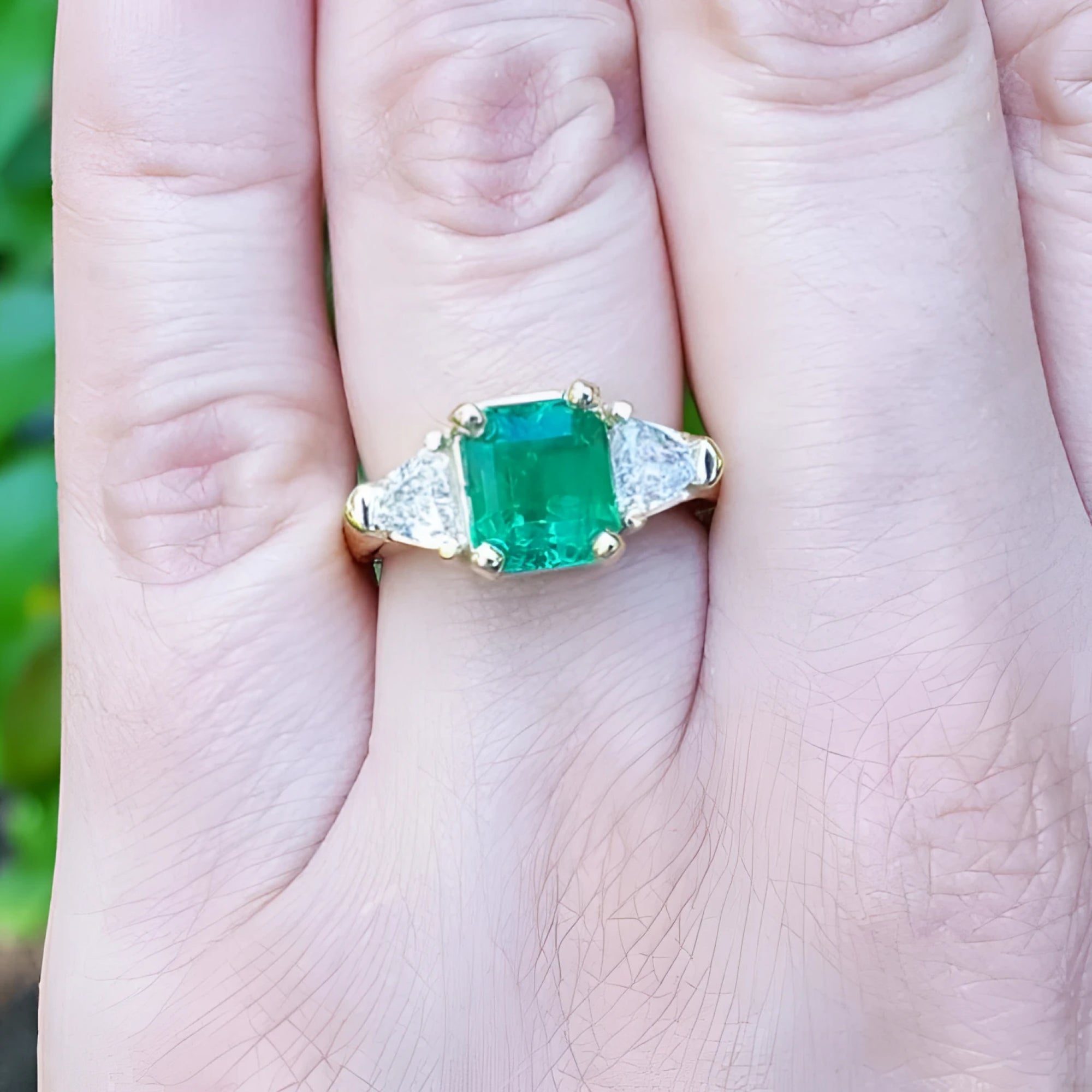 18K yellow gold ring with a GIA certified emerald and side trillion diamonds on a hand.