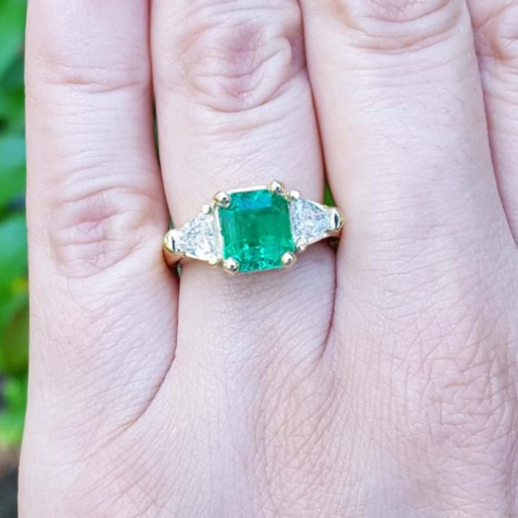 18K yellow gold ring with a GIA certified emerald and side trillion diamonds on a hand.