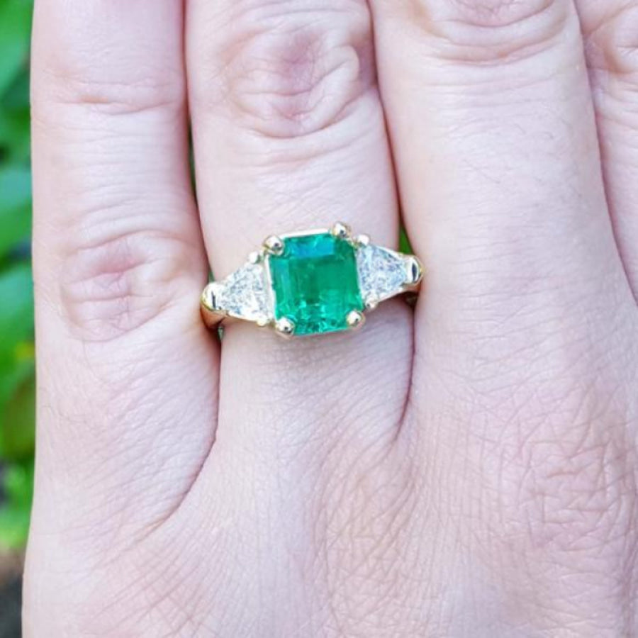 18K yellow gold ring with a GIA certified emerald and side trillion diamonds on a hand.