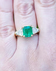 18K yellow gold ring with a GIA certified emerald and side trillion diamonds on a hand.