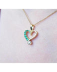 18K yellow gold heart pendant with natural emeralds and a brilliant-cut diamond, worn on a delicate chain.