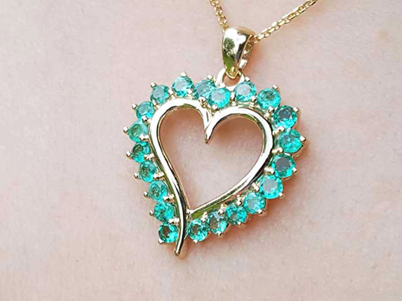 Heart-shaped pendant round colombian emerald stones on a light pink background