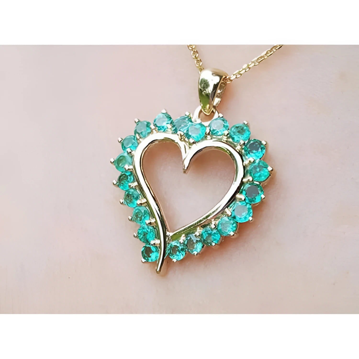 Heart-shaped pendant round colombian emerald stones on a light pink background