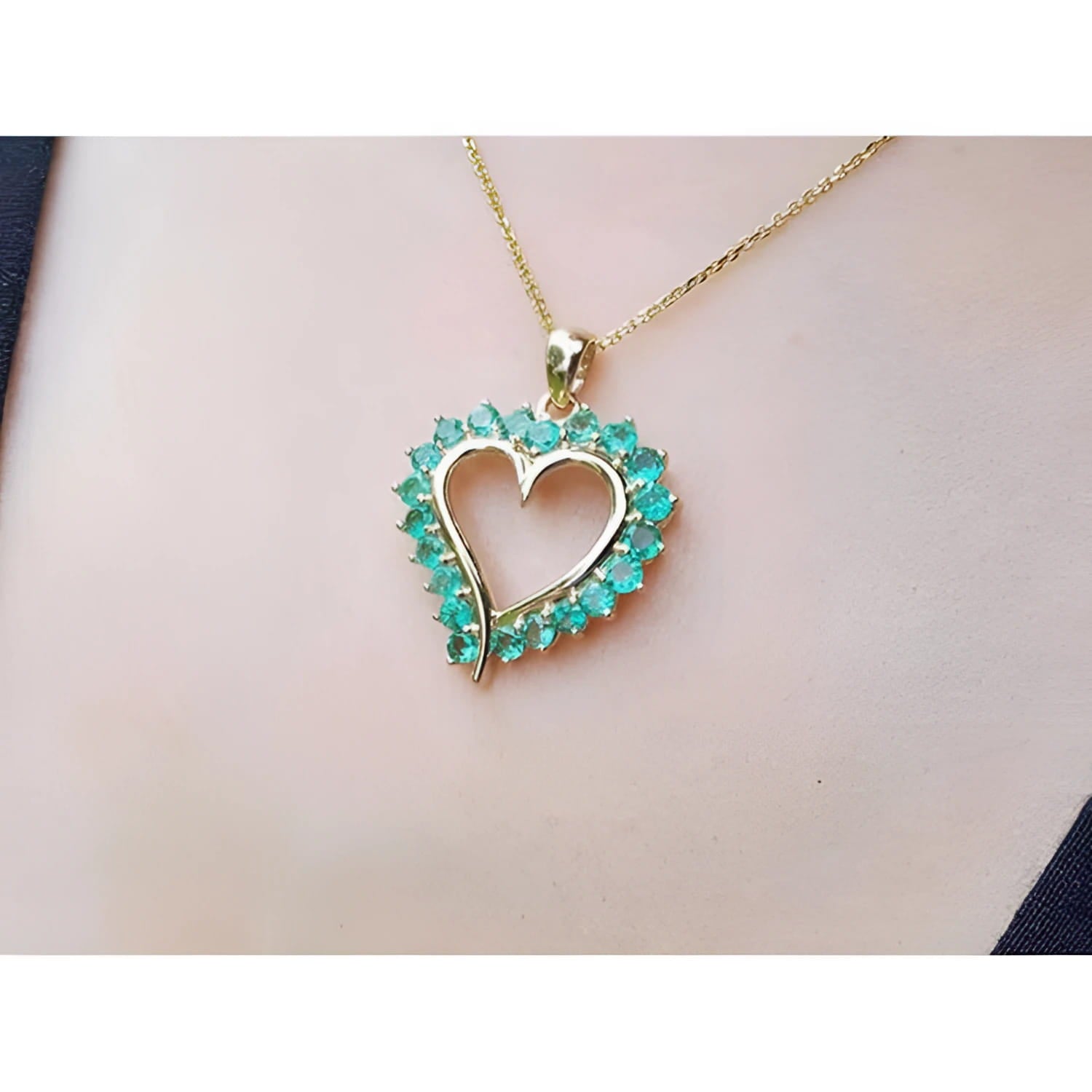 14K gold heart pendant necklace with vibrant green Colombian emeralds, worn on a person.