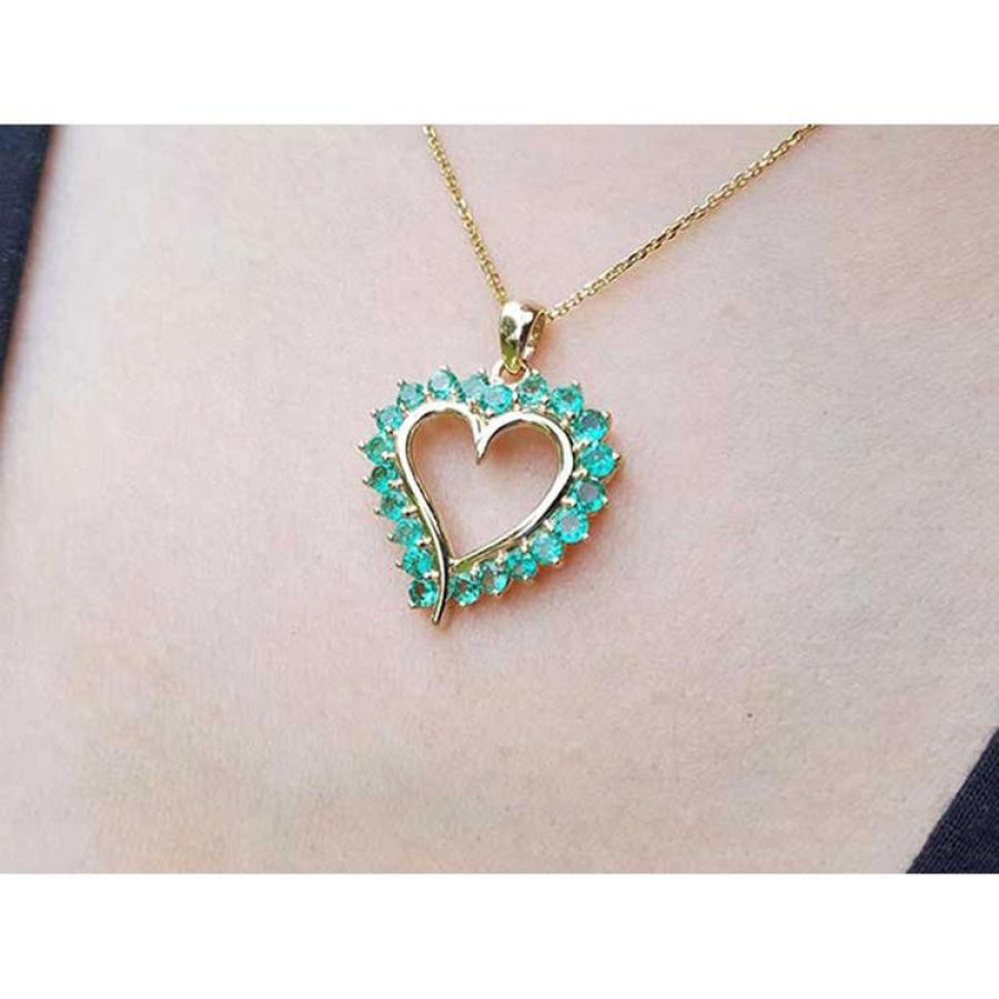 14K gold heart pendant necklace with vibrant green Colombian emeralds, worn on a person.