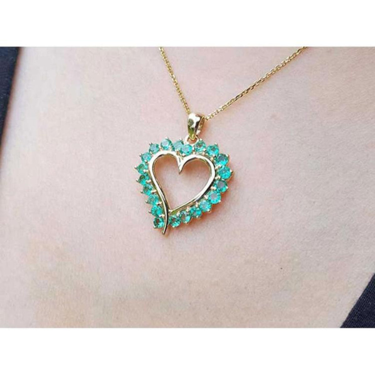 14K gold heart pendant necklace with vibrant green Colombian emeralds, worn on a person.
