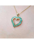 14K gold heart pendant necklace with vibrant green Colombian emeralds, worn on a person.