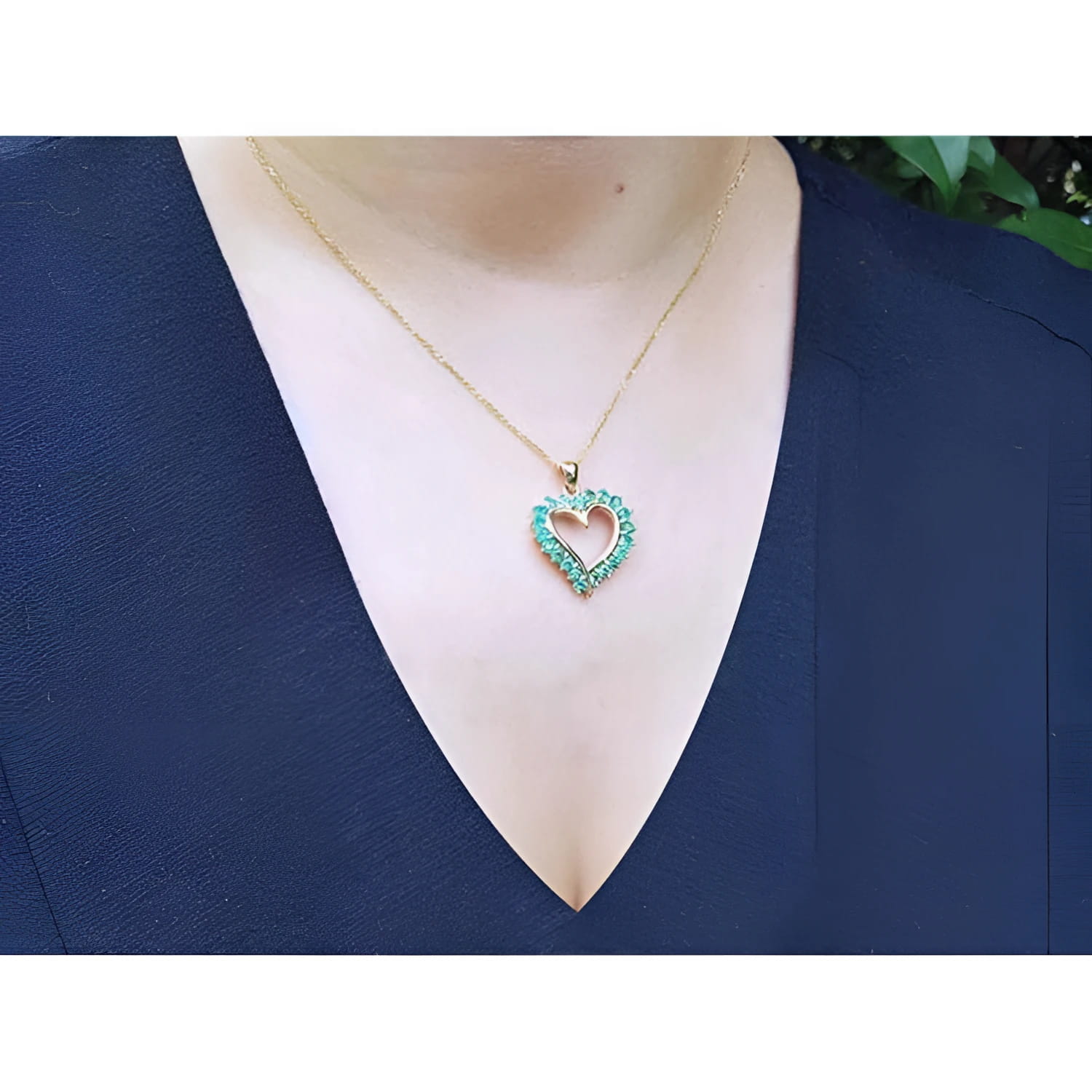 14K gold heart-shaped pendant necklace with vibrant green Colombian emeralds on a woman's chest.