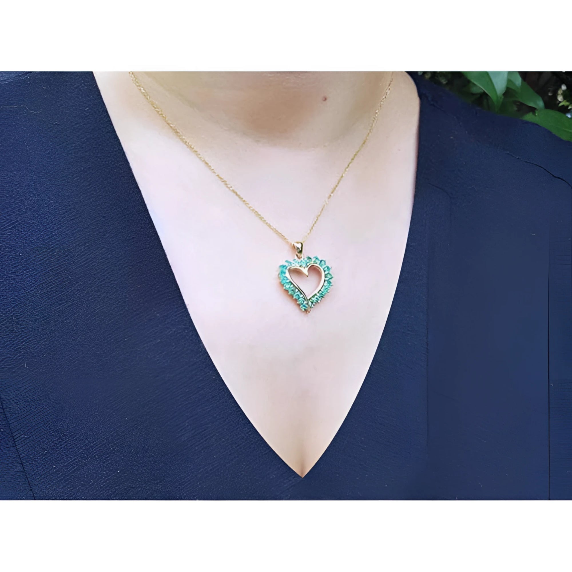 14K gold heart-shaped pendant necklace with vibrant green Colombian emeralds on a woman's chest.