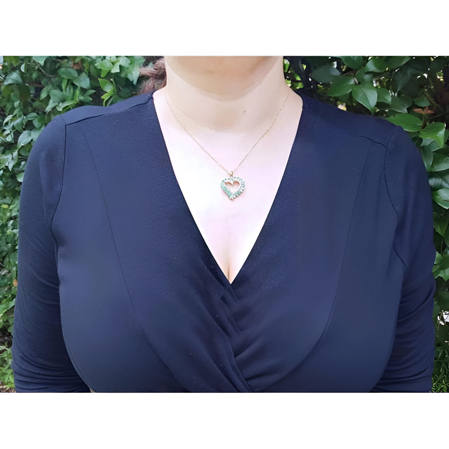 Woman wearing a 14K gold necklace with a heart-shaped emerald pendant.