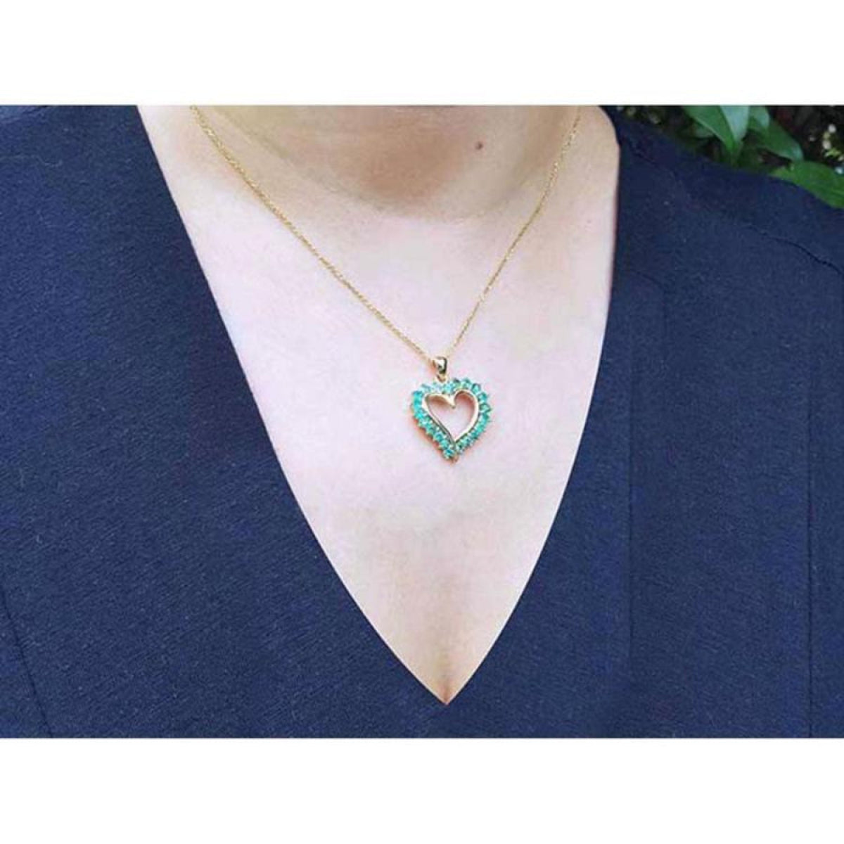 14K gold heart-shaped pendant necklace with vibrant green Colombian emeralds on a woman's chest.