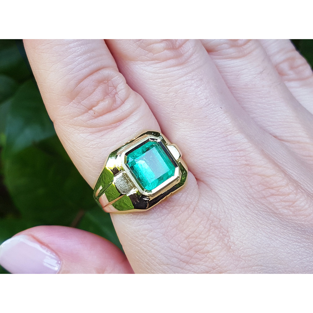 Gold ring with a genuine emerald on a hand against a natural background.