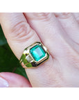 Gold ring with a genuine emerald on a hand against a natural background.