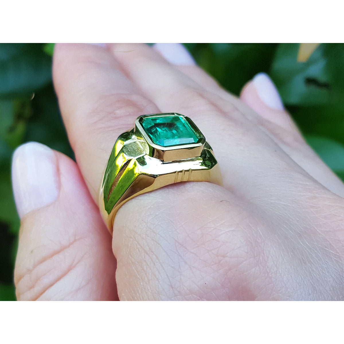 Gold mens ring with a real colombian emerald on a hand against a blurred natural background.