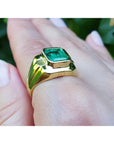 Gold mens ring with a real colombian emerald on a hand against a blurred natural background.