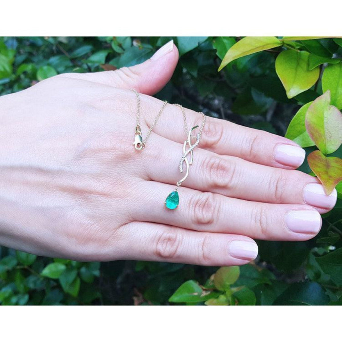 14K yellow gold twisted slider necklace with a pear-shaped emerald pendant on a hand.