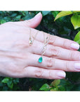 14K yellow gold twisted slider necklace with a pear-shaped emerald pendant on a hand.
