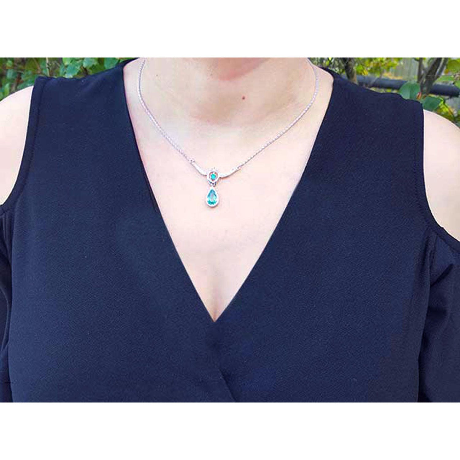 Pear shaped emerald and diamond necklace in 14K white gold on a woman's neck.