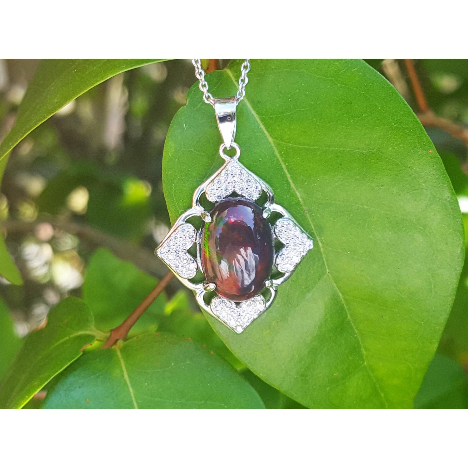 Silver pendant with a black opal on a green leaf background.