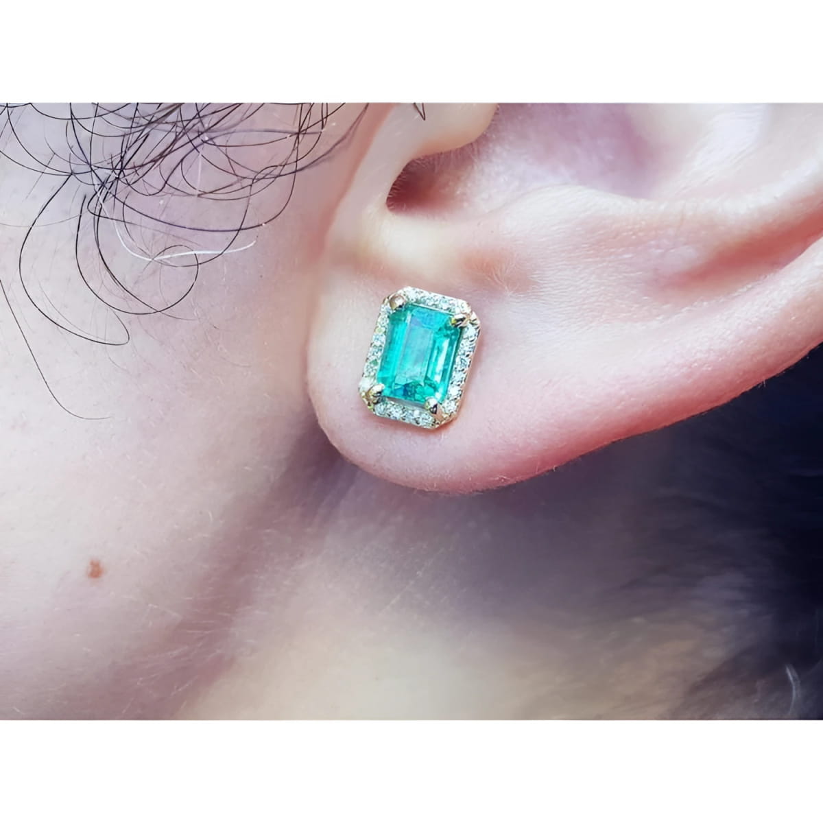 Close-up of a colombian emerald gemstone earring with halo diamond on a person's ear.