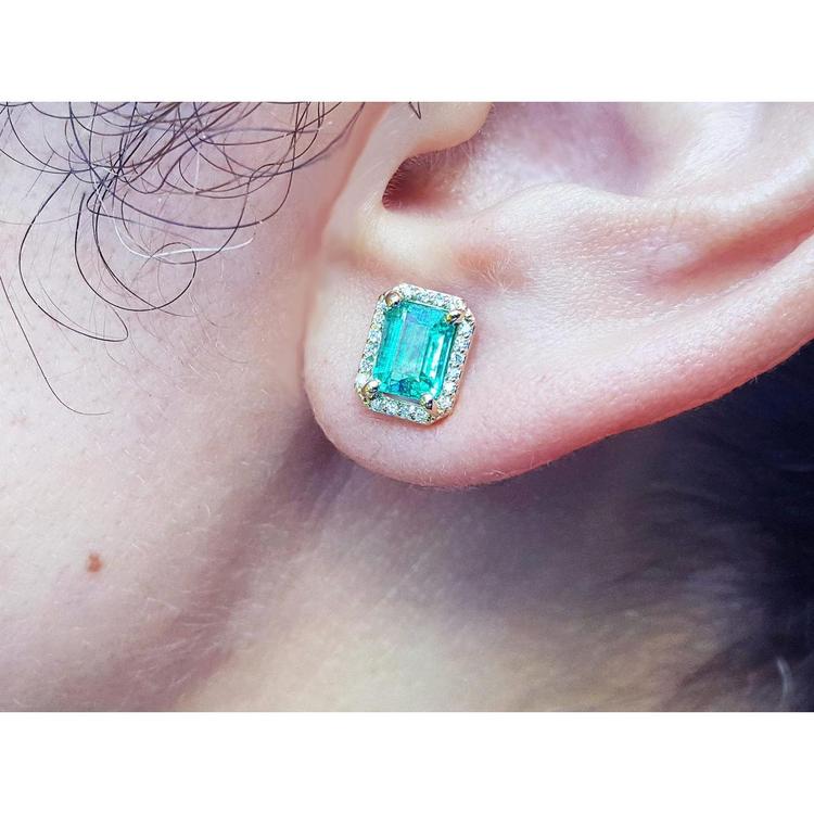 Close-up of a colombian emerald gemstone earring with halo diamond on a person's ear.