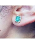 Close-up of a colombian emerald gemstone earring with halo diamond on a person's ear.