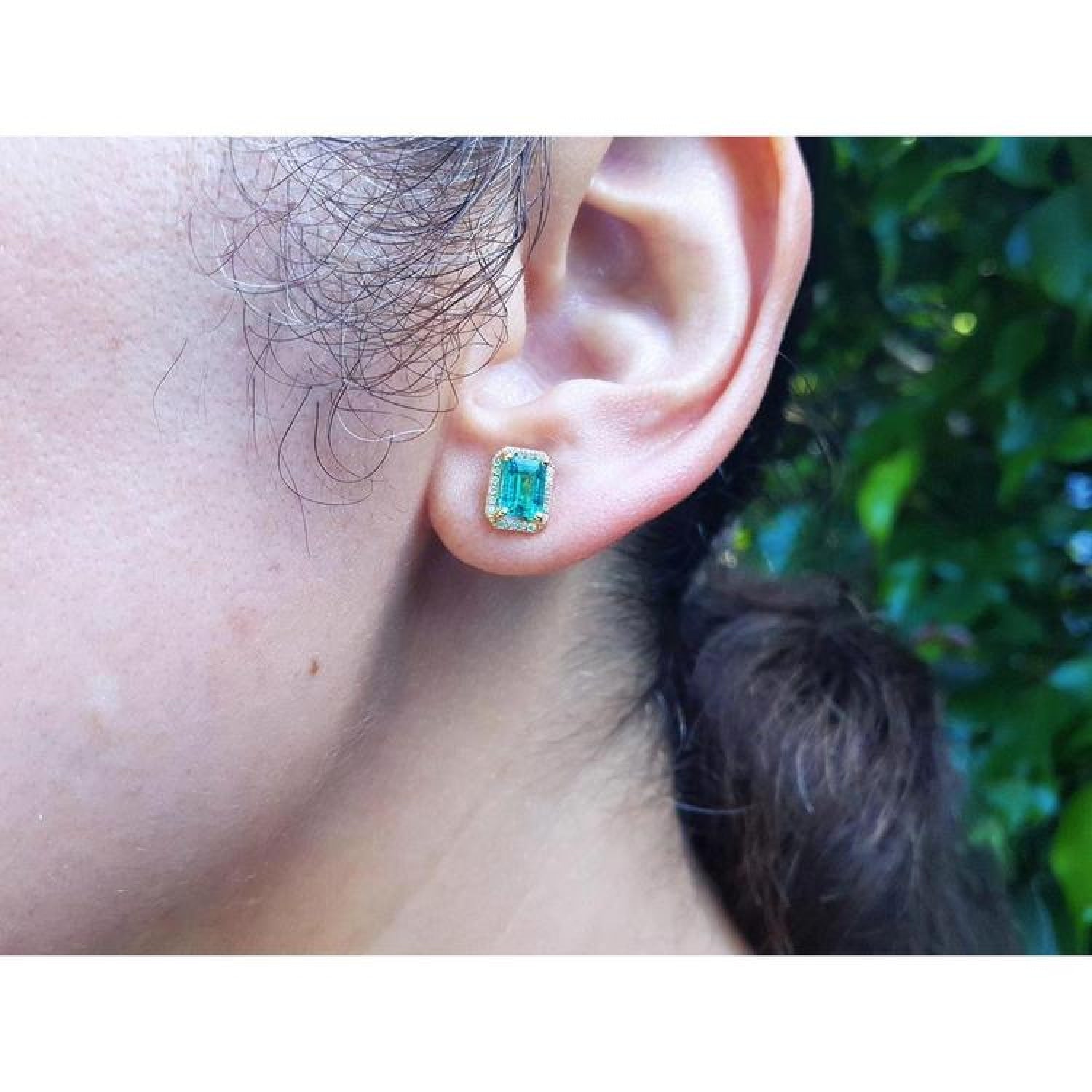 Emerald stud earring with diamond halo in 14k yellow gold on an ear.