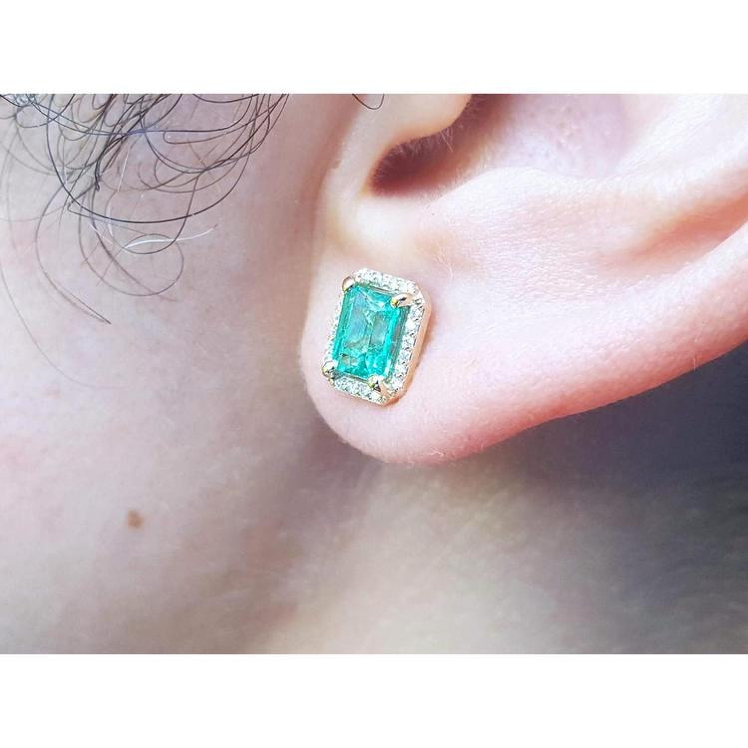 Emerald stud earring with diamond halo in 14k yellow gold on an ear.