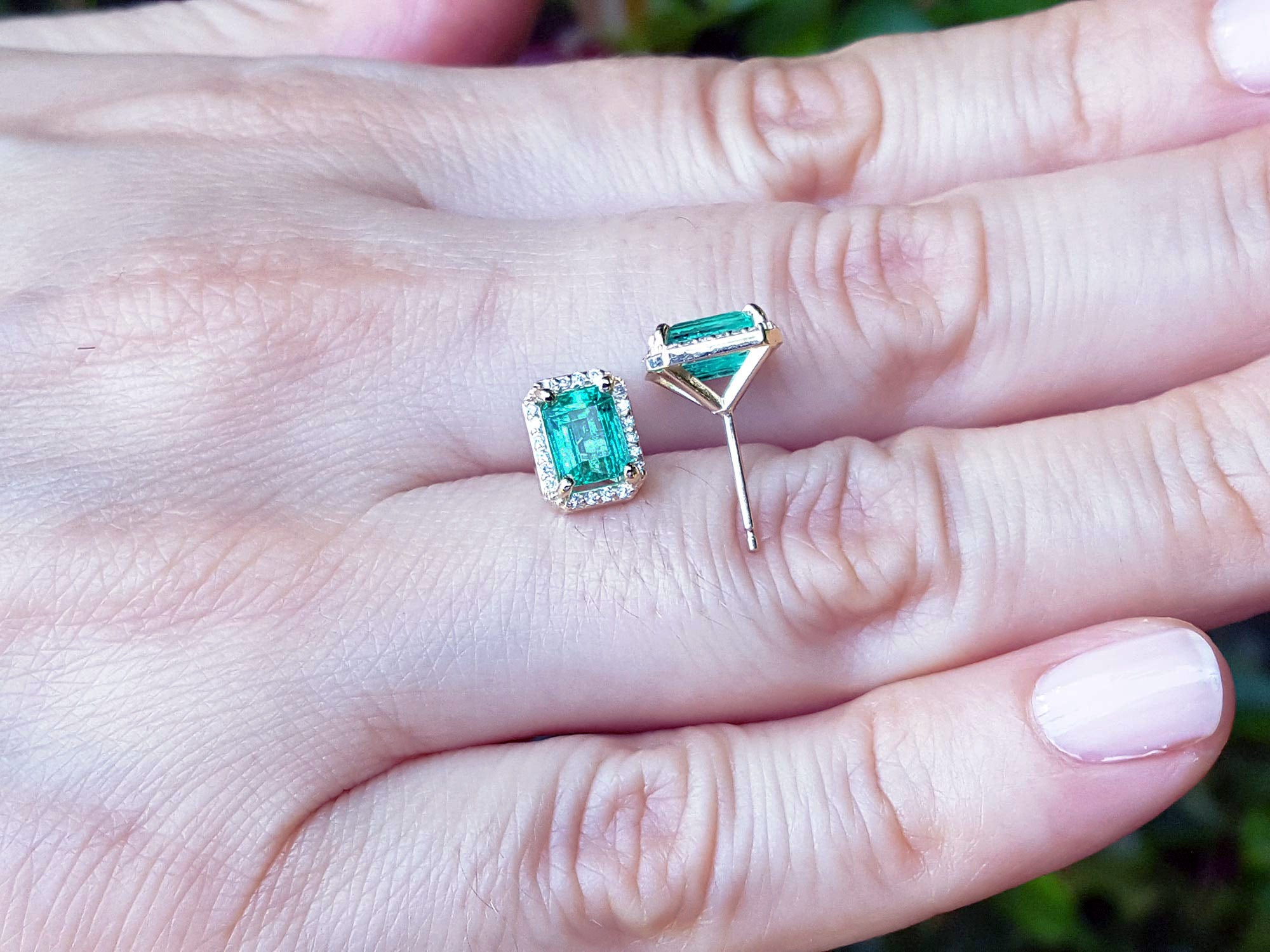 Natural emerald stud earrings displayed on a hand