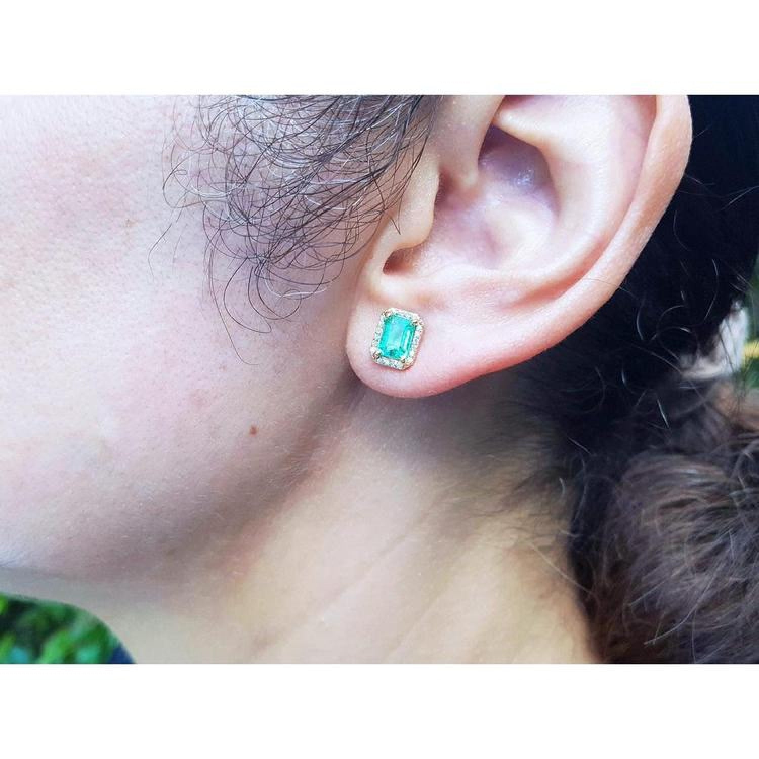 Emerald stud earring with diamond halo in 14k yellow gold, worn on an ear.