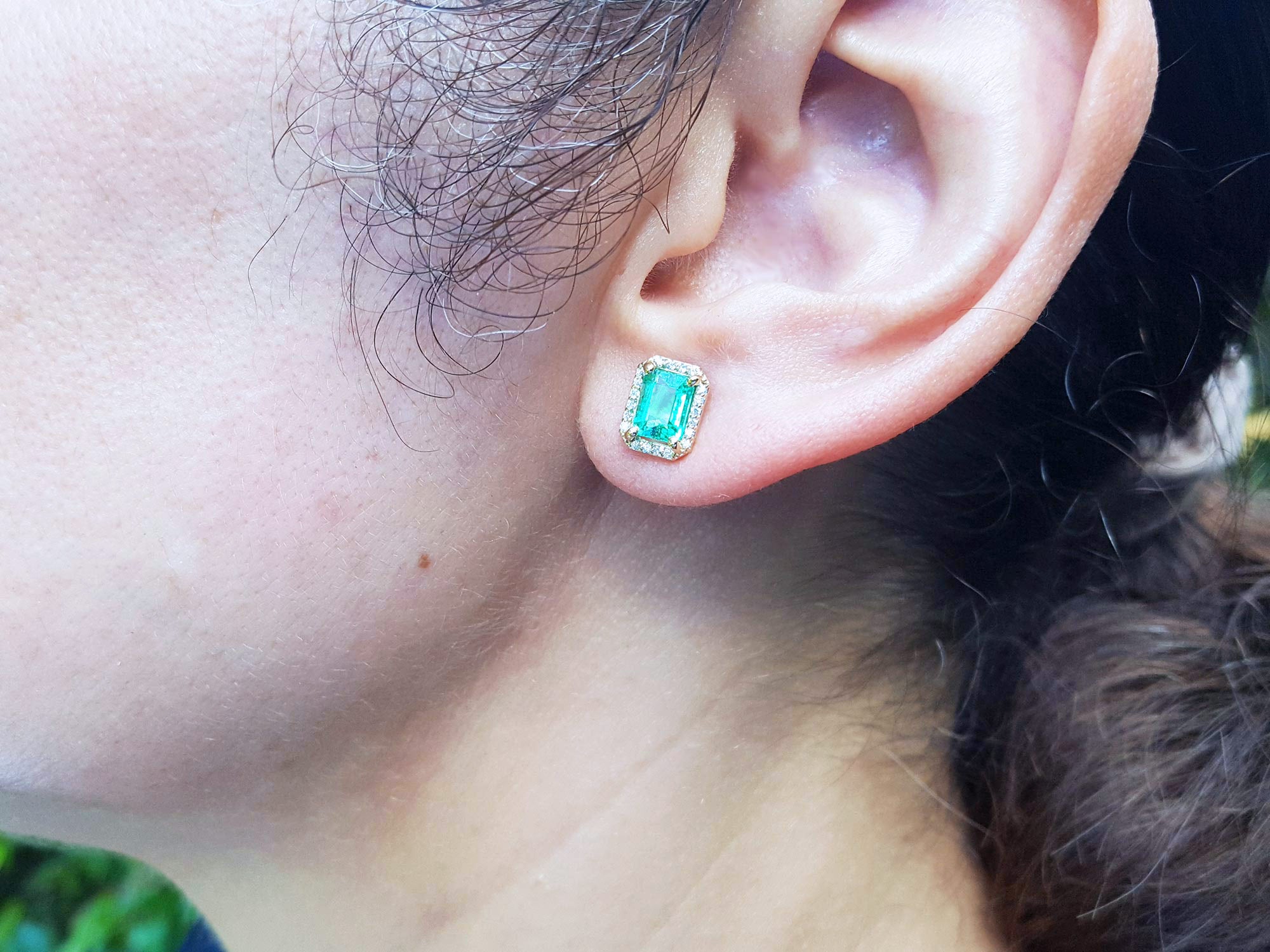 Close-up of an ear wearing a genuine emerald stud earring.