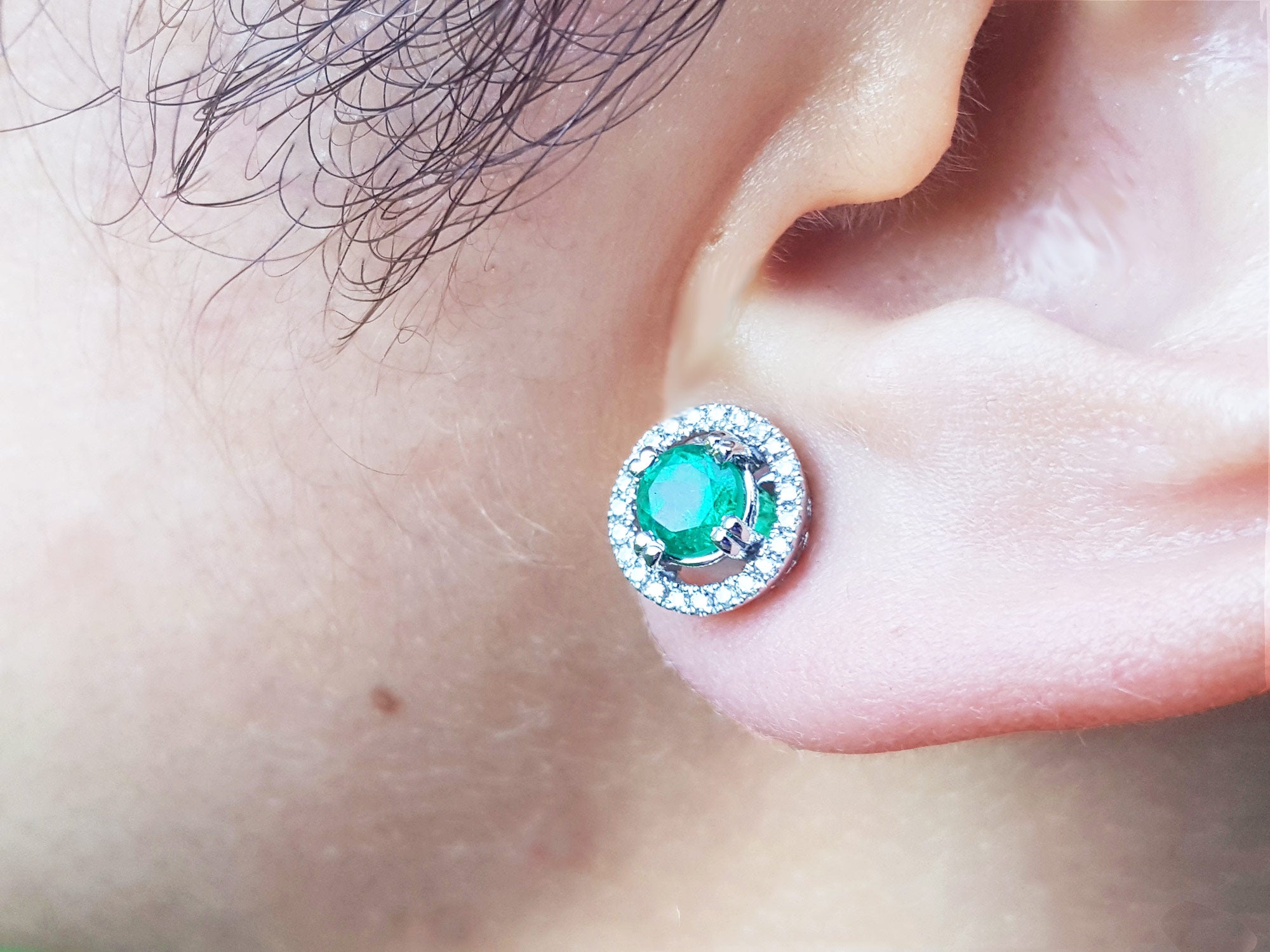 Close-up of an ear wearing halo diamond emerald stud earring.