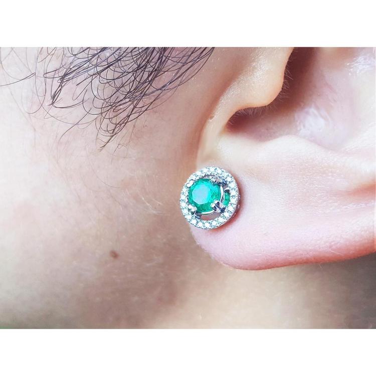 Close-up of an ear wearing halo diamond emerald stud earring.