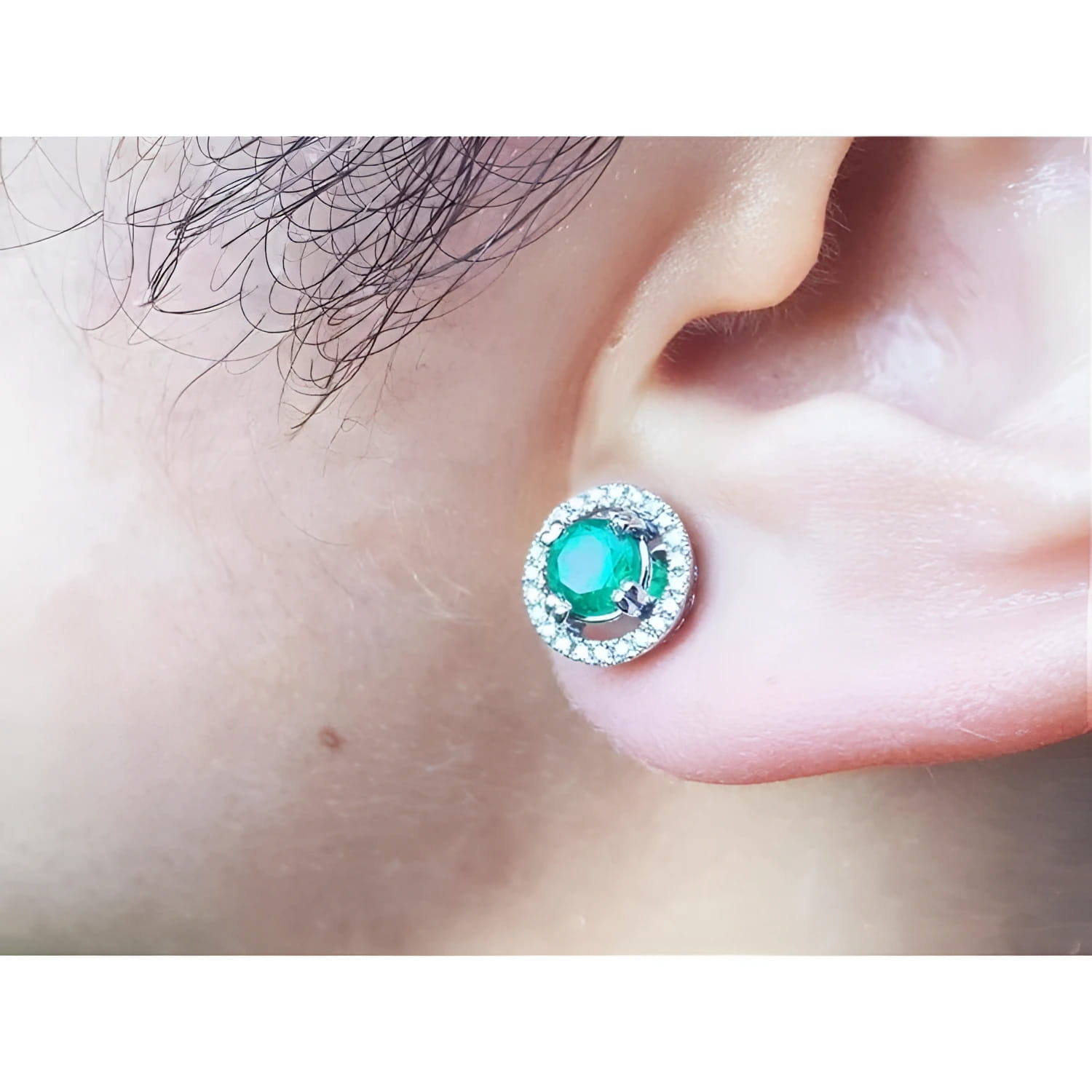 Close-up of an ear wearing halo diamond emerald stud earring.