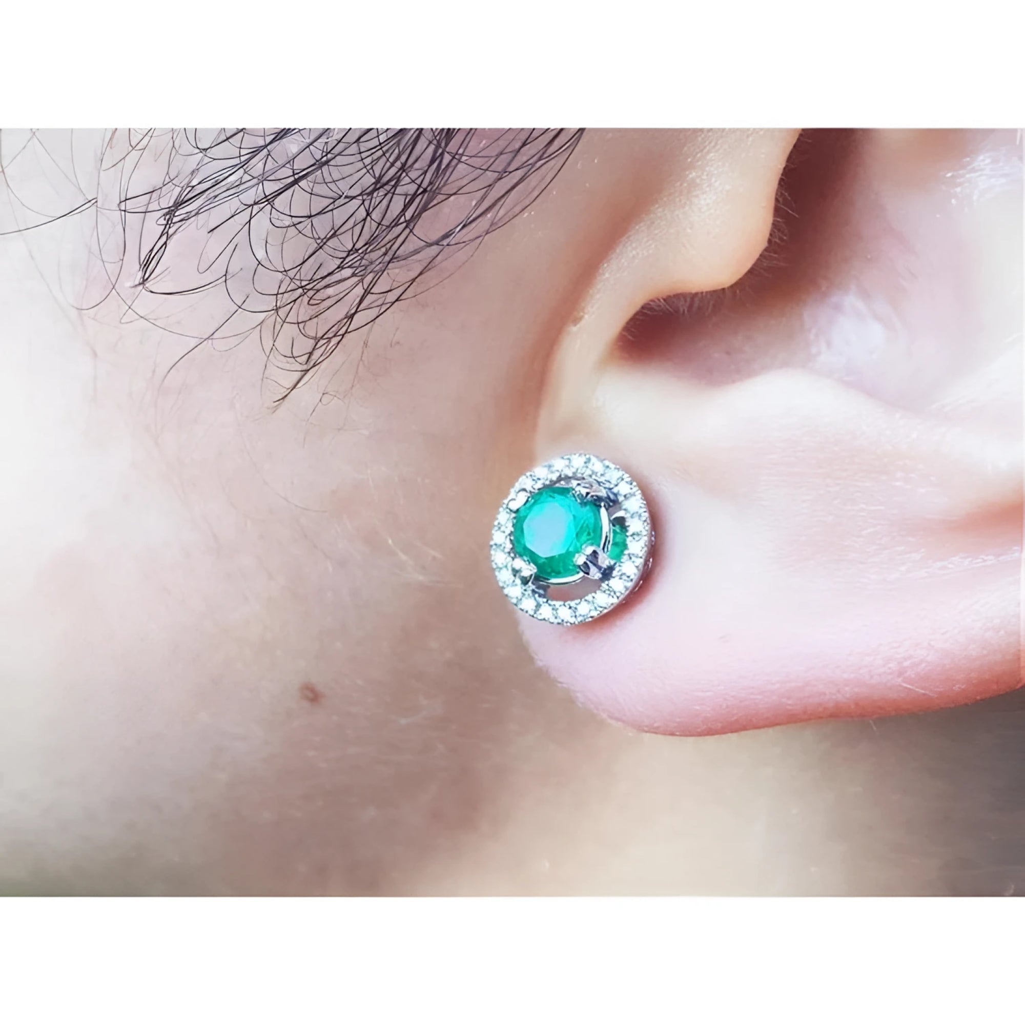 Close-up of an ear wearing halo diamond emerald stud earring.