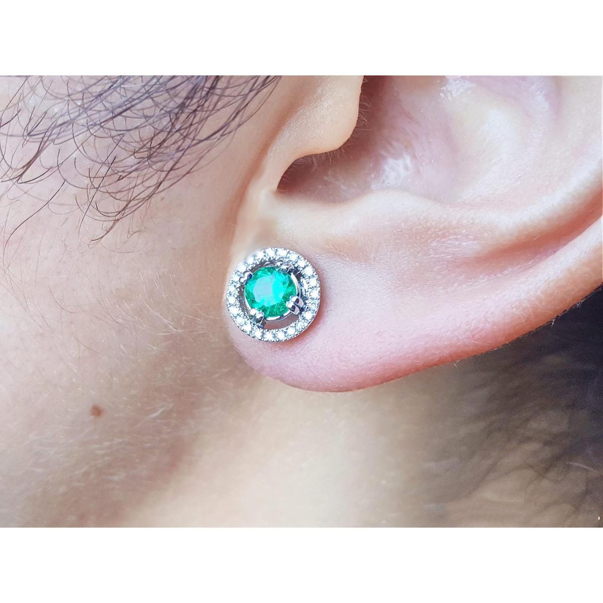 Close-up of an ear wearing a natural halo diamond emerald stud earring,