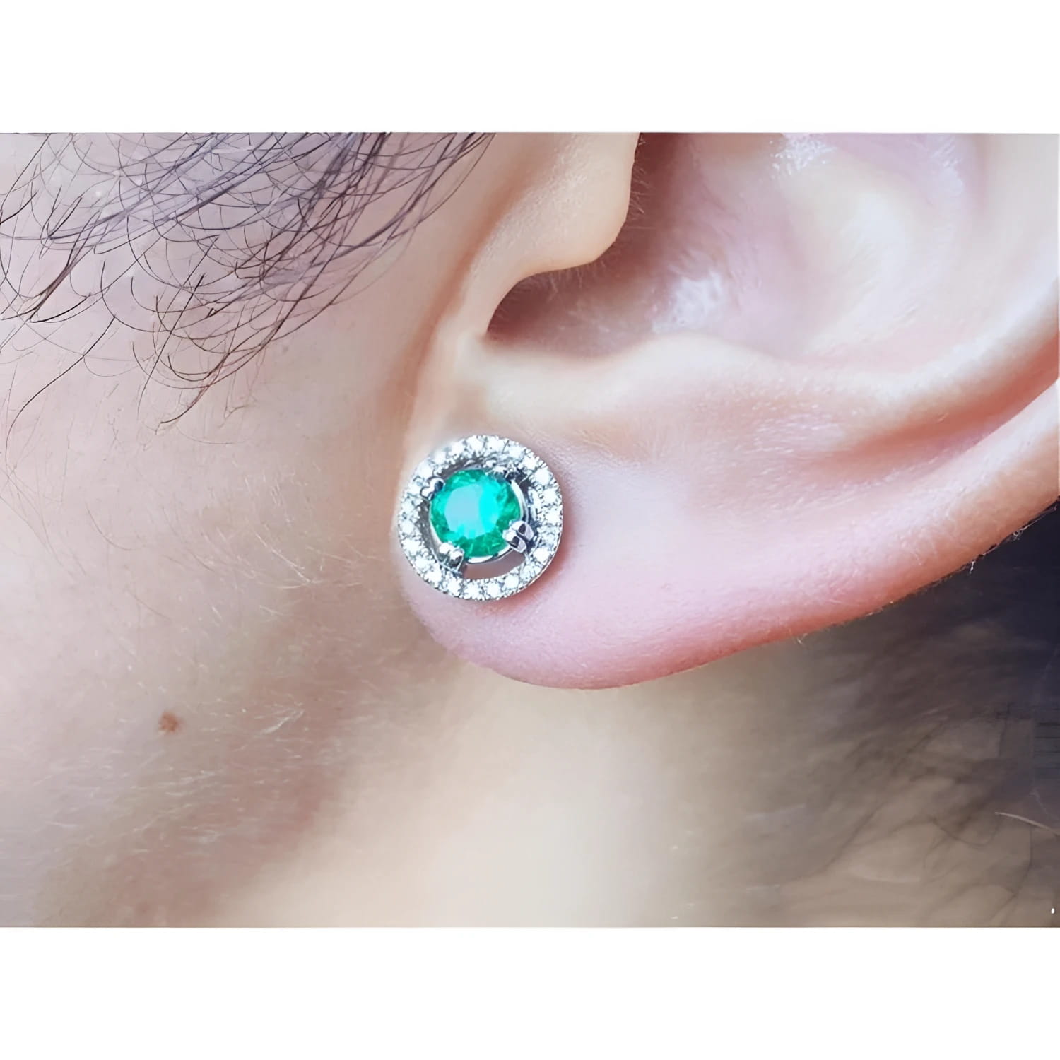 1.06 ct deep bluish-green Colombian emerald stud earring with diamond halo and secure screw back on an ear.