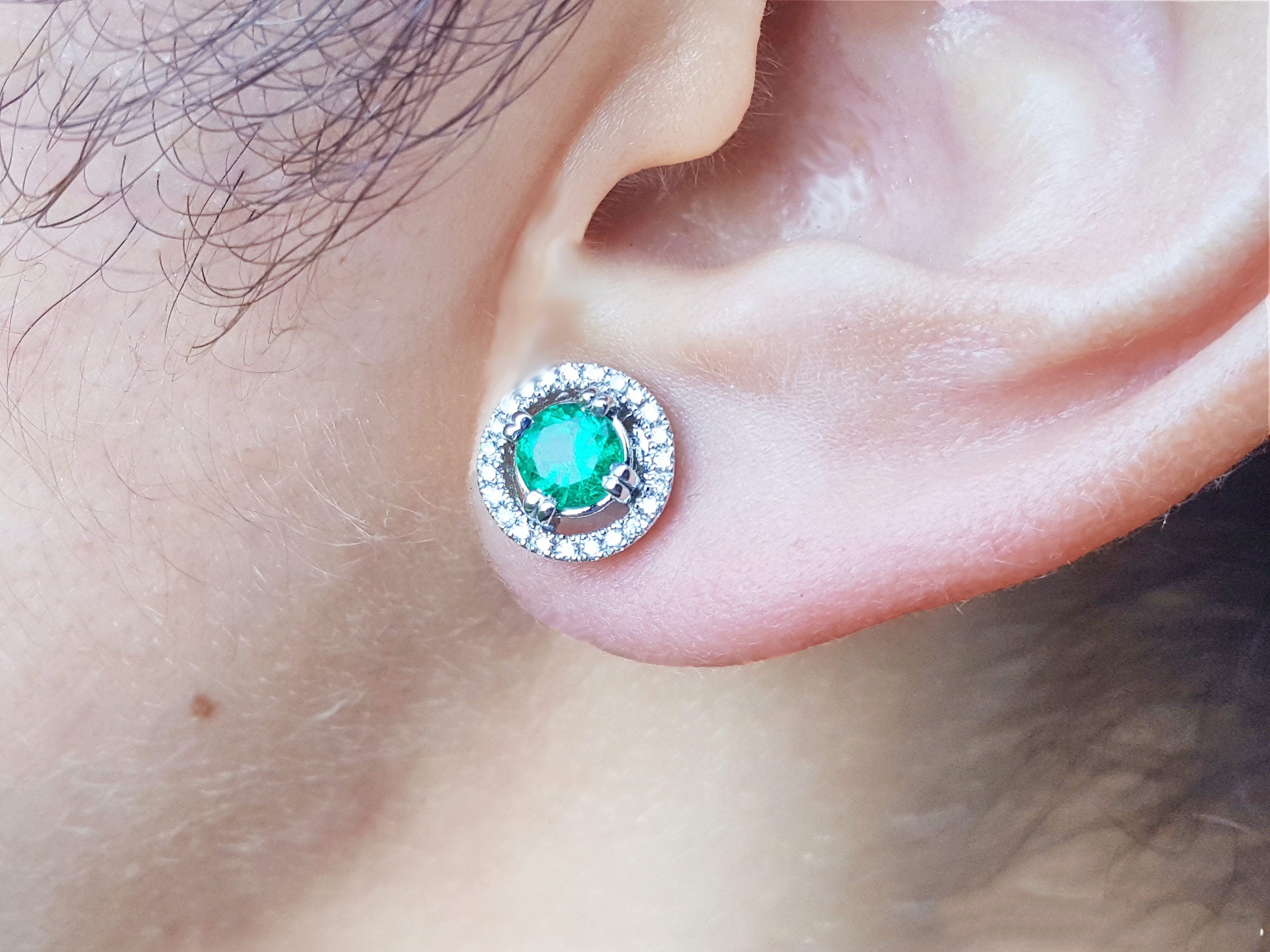 Close-up of an ear wearing a natural halo diamond emerald stud earring,