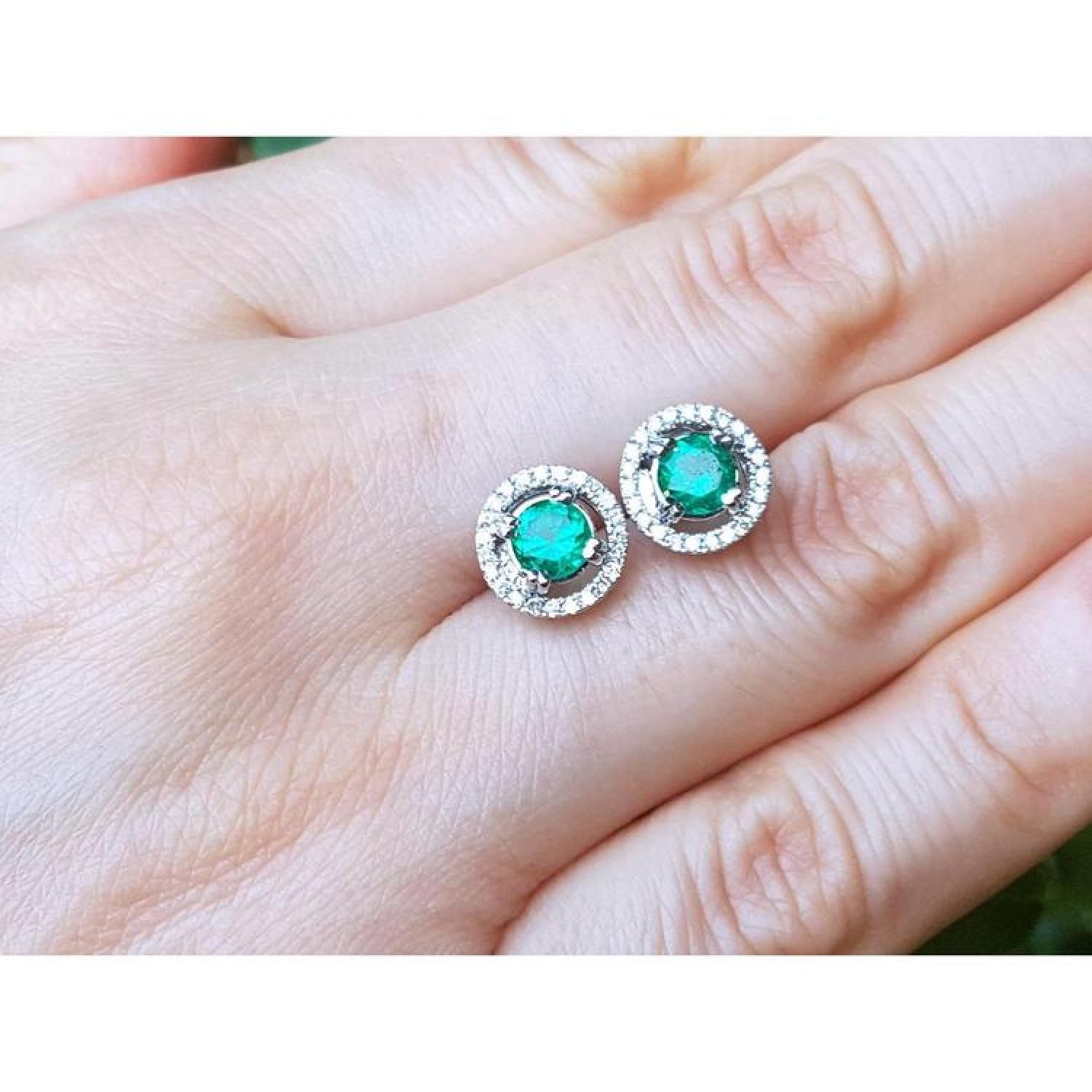 Halo emerald stud earrings with deep bluish-green emeralds encircled by diamonds, set in 14K white gold.