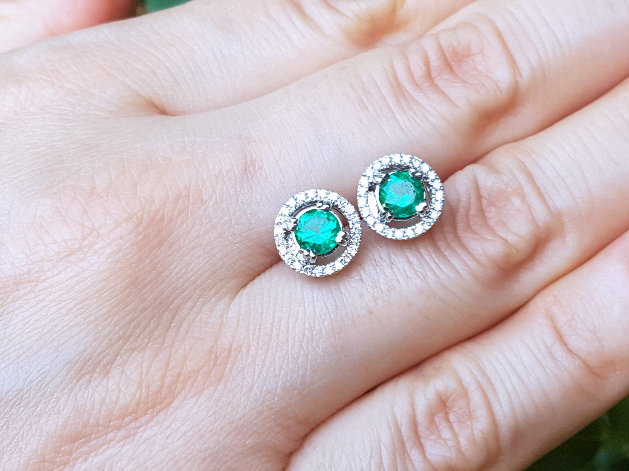Pair of emerald stud earrings on a hand.