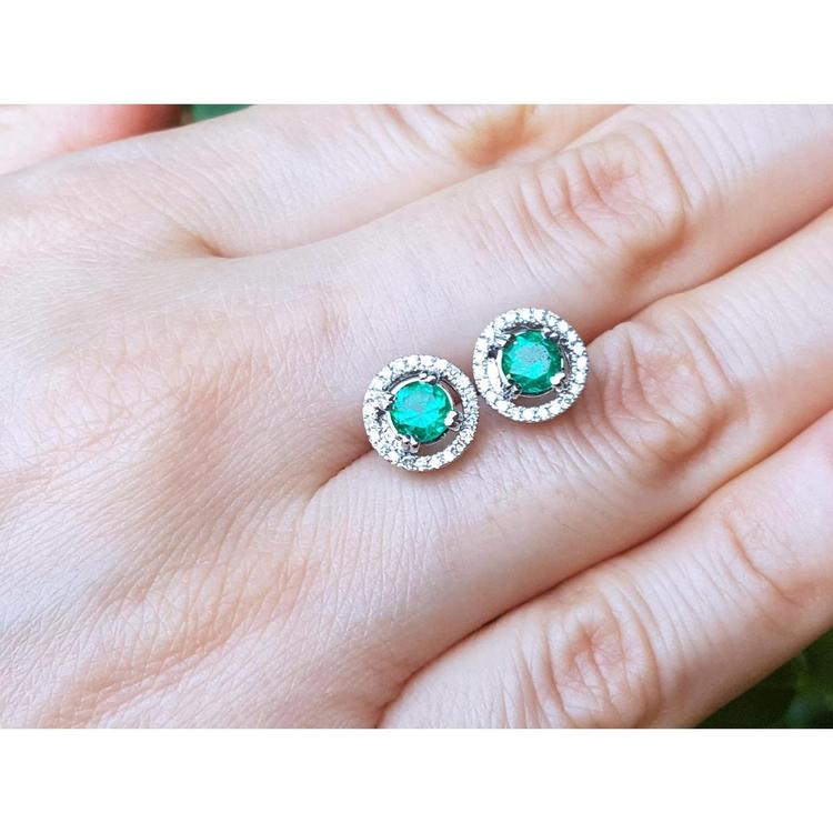 Pair of emerald stud earrings on a hand.