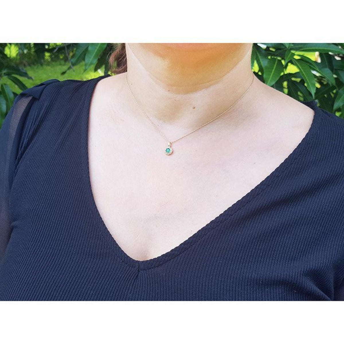 Minimalist 14K yellow gold necklace with a round cut green emerald and small diamond accents, worn on a woman.