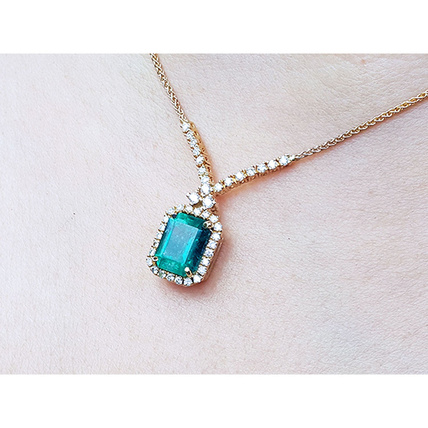 14K yellow gold halo necklace with a rectangular bluish-deep green emerald and natural diamonds.