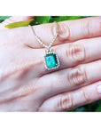 Emerald halo necklace with natural diamonds on a 14K yellow gold chain, held by a hand.