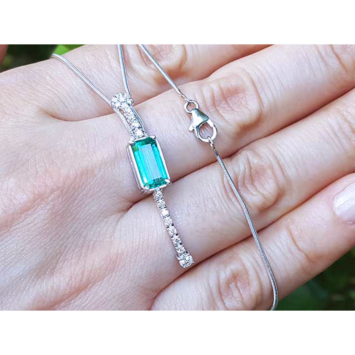 Lariat white gold necklace with a natural emerald gemstone held in a hand against a blurred background